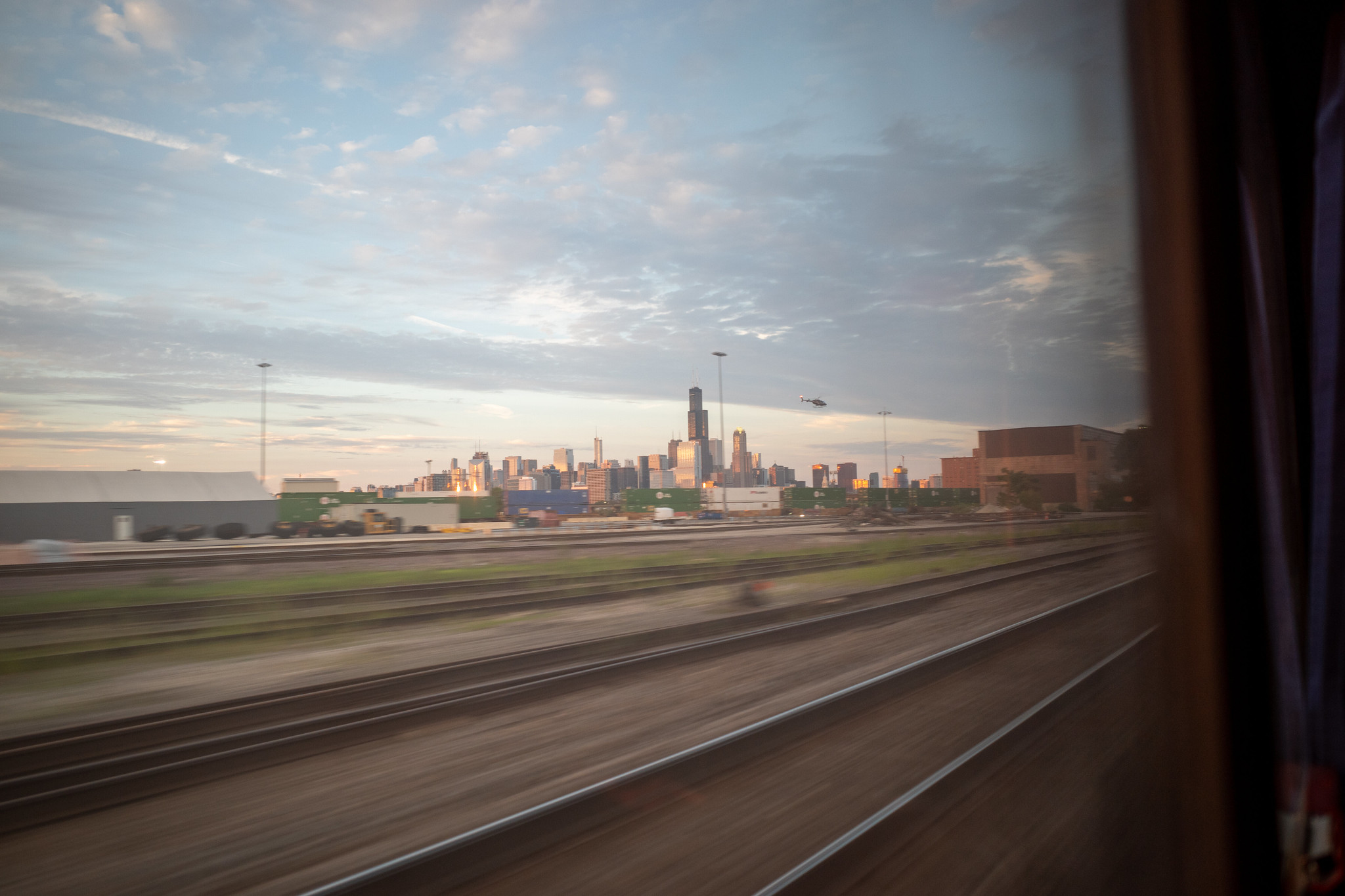The distant Chicago skyline stands tall beyond a helicopter and the motion blurred train tracks