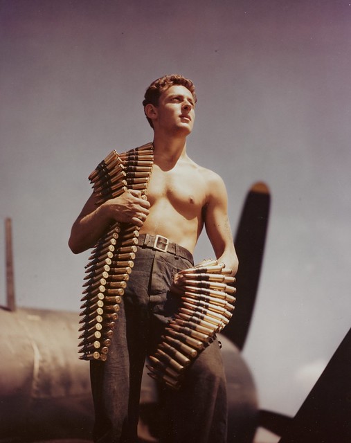 Aviation Ordnance man N F Nitishin, Carries belts of 50cal. Machine gun ammunition, as he prepares to arm the guns of a VOUGHT F4U-1 Corsair Base fighter at a pacific Base, circa 1944-45.