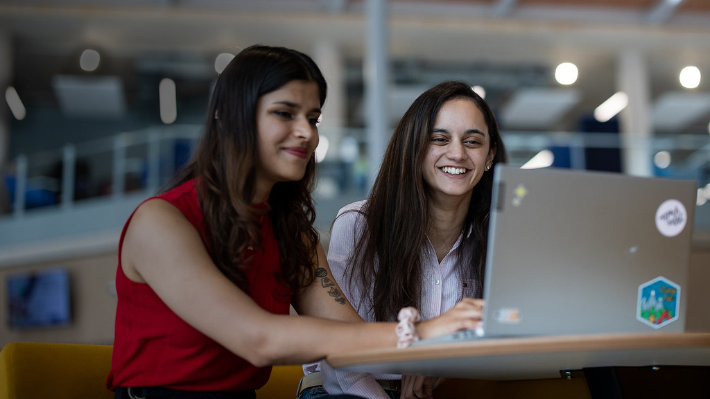 Two students smiling and looking at a laptop