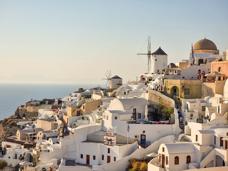 A view of the white houses in Santorini at sunset. In prim plan there are two windmills