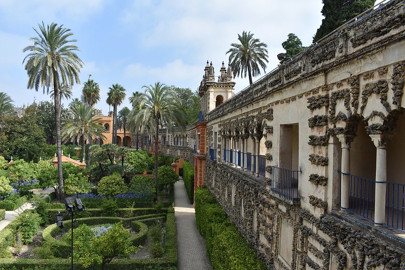A photo of the Alcazar of Seville, with the building on the right side and the gardens on the left side.