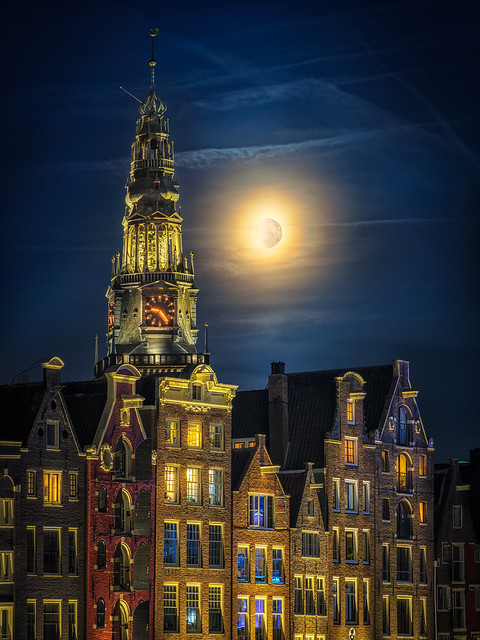 The old church on the Damrak in Amsterdam with boats and the moon during the bluehour