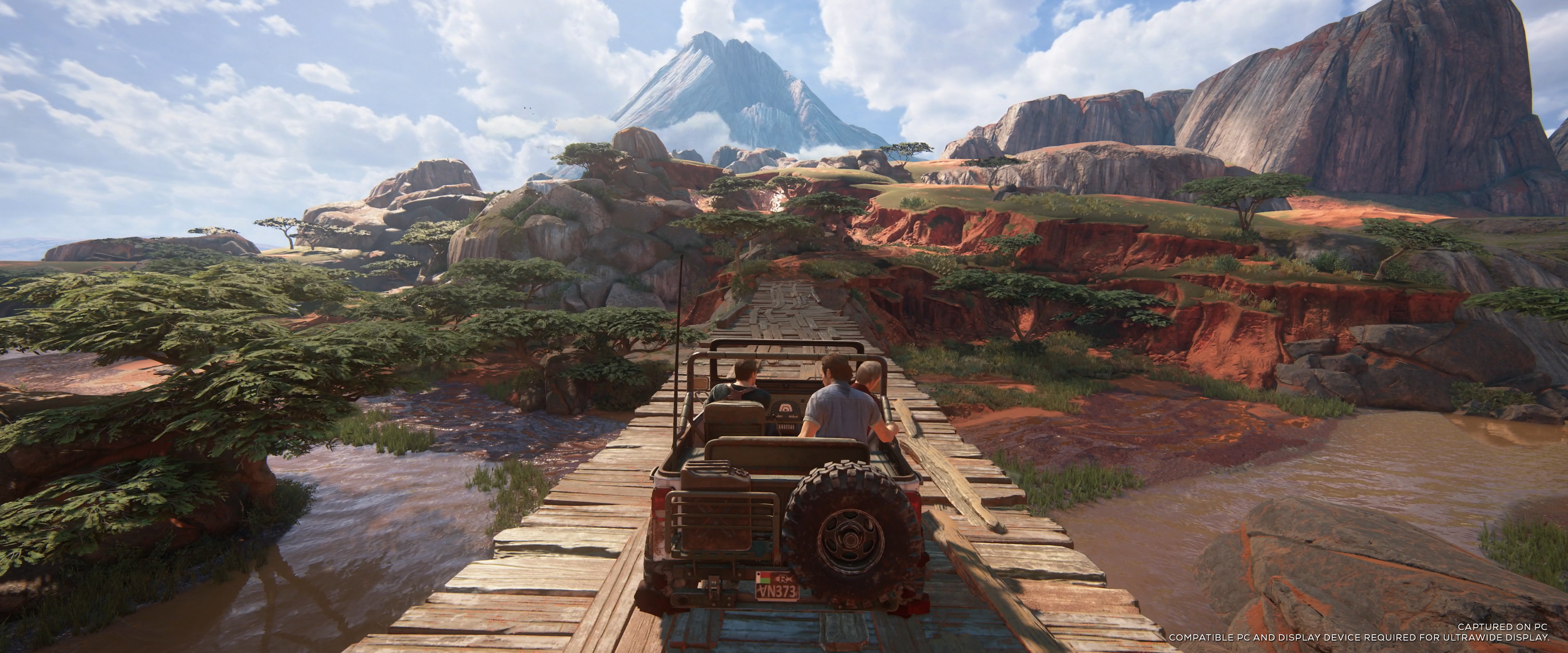 Au premier plan, une jeep fonce sur un pont en bois, avec un paysage luxuriant qui s'étend à perte de vue. PC et écran compatible requis pour l'affichage en ultra large.