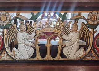 light shining through angels holding the letter M (Ninian Comper, 1913)
