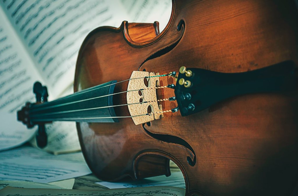 dramatic closeup of cello on its side with music scores in background - Musician's Way Newsletter