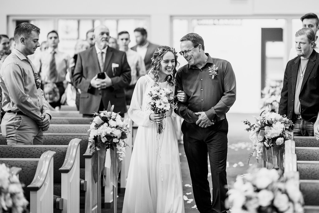 DAD TELLING HIS DAUGHTER A JOKE AS THEY WALK DOWN THE AISLE