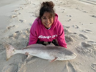 Photo of woman sitting in the sand with a large fish she caught
