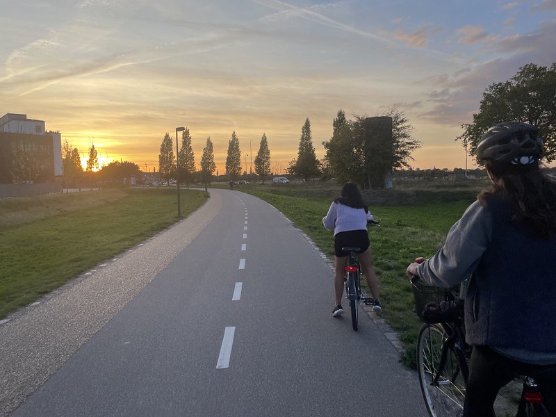 Two people bike down a curved bike path while the sun sets ahead of them.