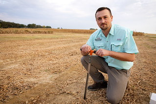 Gerson Drescher kneels in a harvested field with a core soil sample extraction tool.