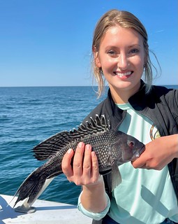 Photo of woman on a boat holding up a black sea bass