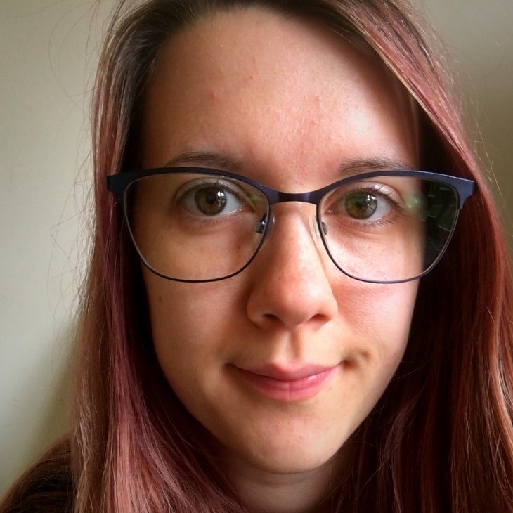 A photo of Tricia. She is wearing black rimmed glasses and has light red hair.