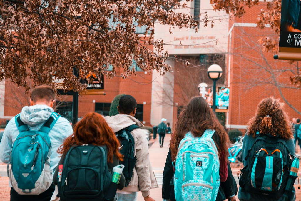 Five students strolling towards a college building, backpacks slung over their shoulders, their backs turned to the camera - Top 10 Facts You Need to Know About the FAFSA