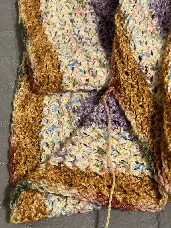a close-up view of semi-folded cardigan fabric showing stripes of extended single crochet stitches in dark golden yellow, speckled pink/white/yellow/blue, and lilac