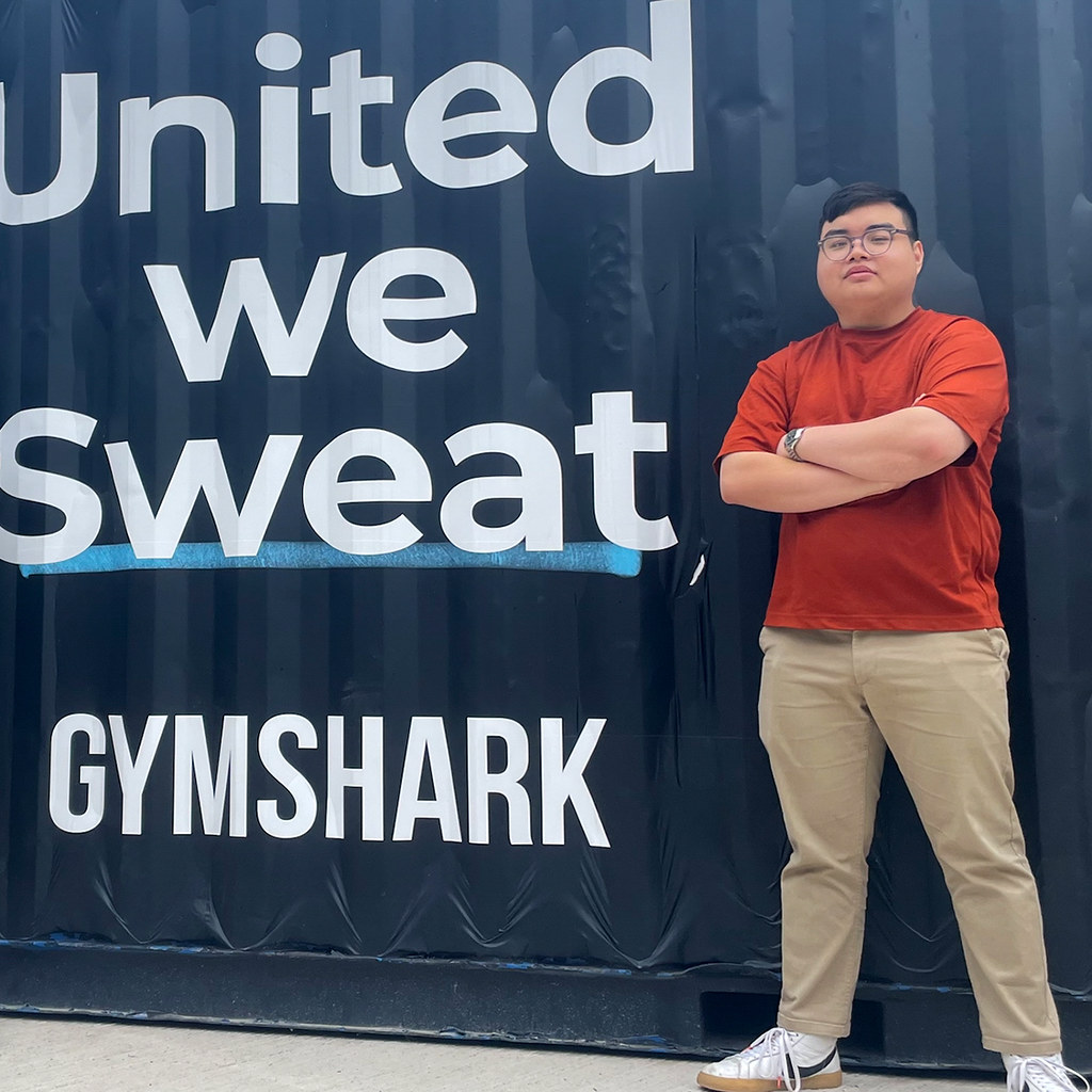 A young man standing next to a shipping container with the Gymshark logo on it.