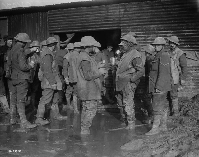 Canadian soldiers in trench waders outside a free coffee stall /  Soldats canadiens en uniforme des tranchées, devant un comptoir où l’on sert du café gratuit
