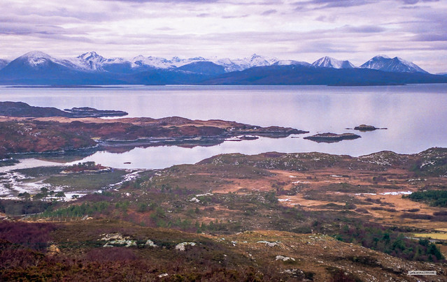 The sublime, colourful beauty of the West Coast of Scotland. View from Creag an Garadh, above Plockton, to the bay called Bagh an t-Strathaidh near Duirinish with Portneora on the headland. Black and Red Cuillins, under snow, on the Isle of Skye.