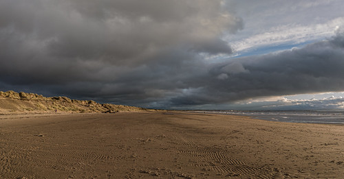 A photo of a wide, sandy beach with dunes on the left.