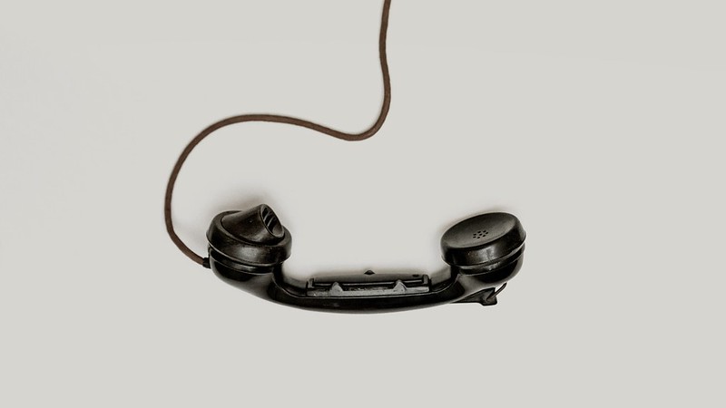 A black telephone receiver with a wire on a white background.