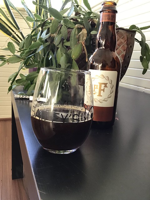 Pfriem's maple barrel aged smoked porter, in glass on table, with bottle of same behind that glass. 