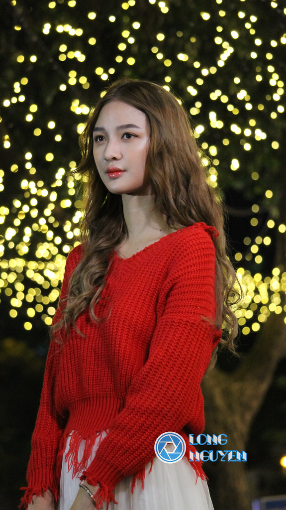 A charming beautiful girl whose shiny curly blonde hair is posing gracefully with a red sweater and a white skirt in Christmas spirit.