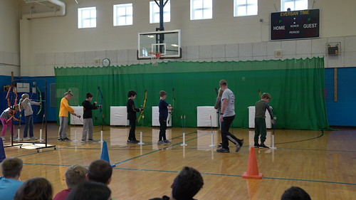 Students in a gymnasium shoot arrows at targets
