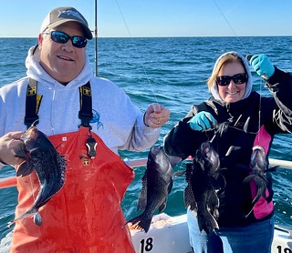 Photo of man and woman on a boat, each holding one or more sea bass on a line