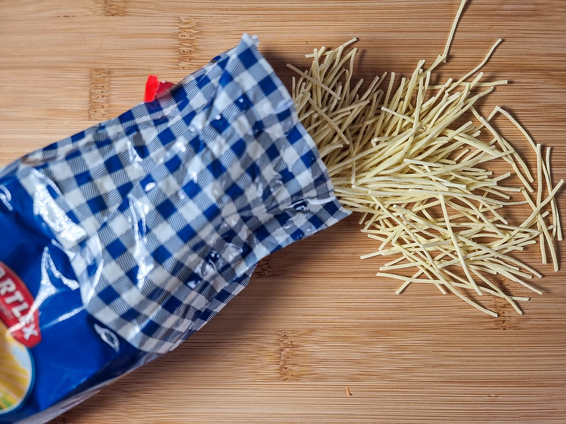 Thin and short noodles on a chopping board, coming out of a blue pack.