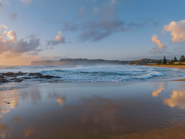 Surfs up at the beach with scattered clouds and reflections