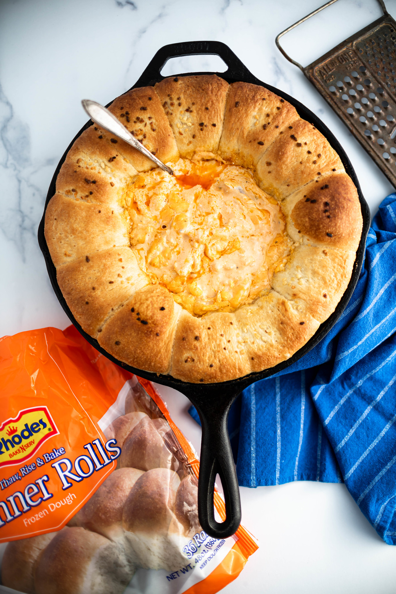 Cast iron skillet with rhodes rolls around the edge with buffalo chicken dip in the middle.