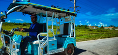 Yaguajay city, an electric bike rolling through Circuito Norte road with '4 de Abril' neighborhood recently created with the Venezuelan petrocasa (oil-house) technology. Sancti Spiritus, Cuba, September 2022