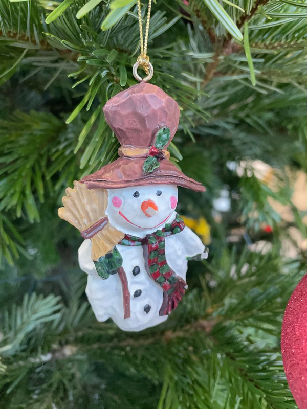 Cheery snowman ornament hanging from a spruce evergreen tree