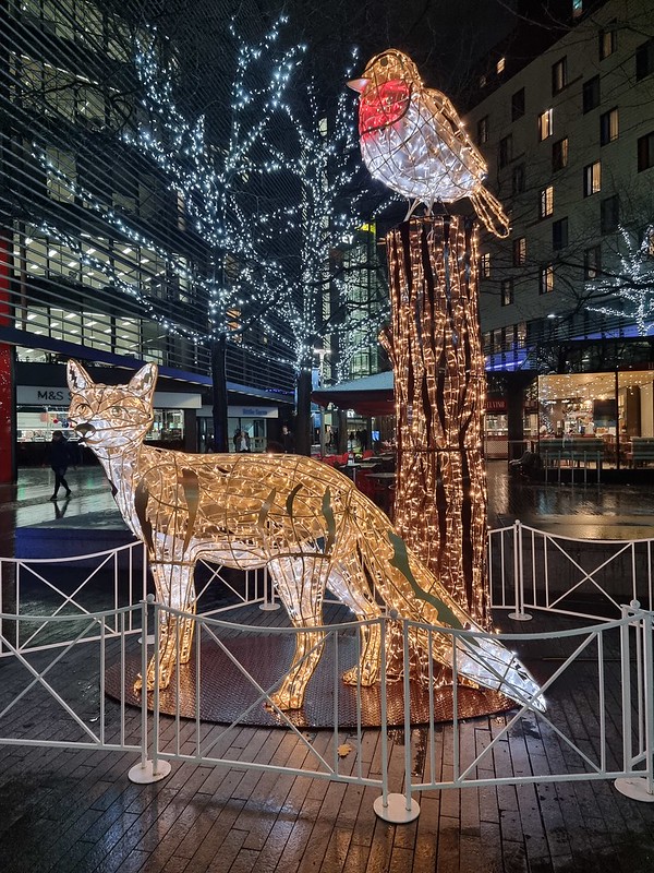 A giant fox near a tree with a robin on it made from yellow lights