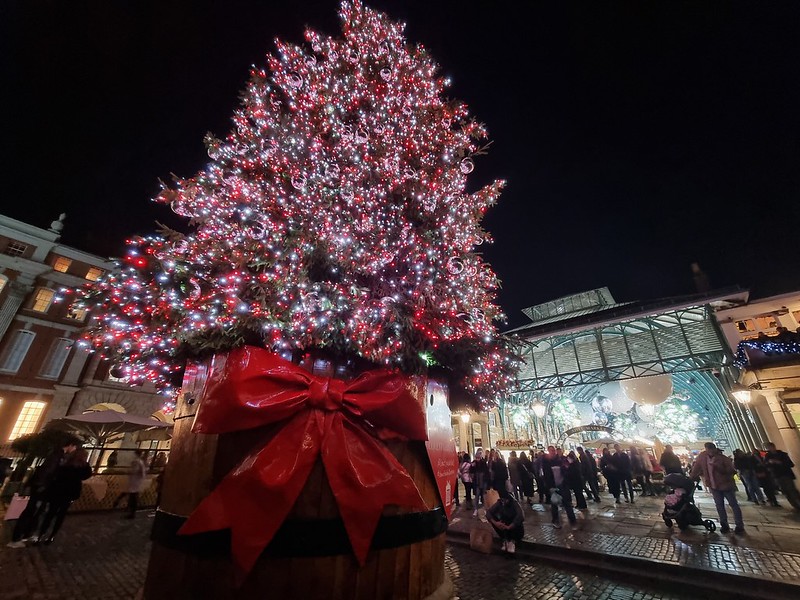 The large Christmas tree in Covent Garden, decorated with red lights and having a giant red ribbon at the bottom.