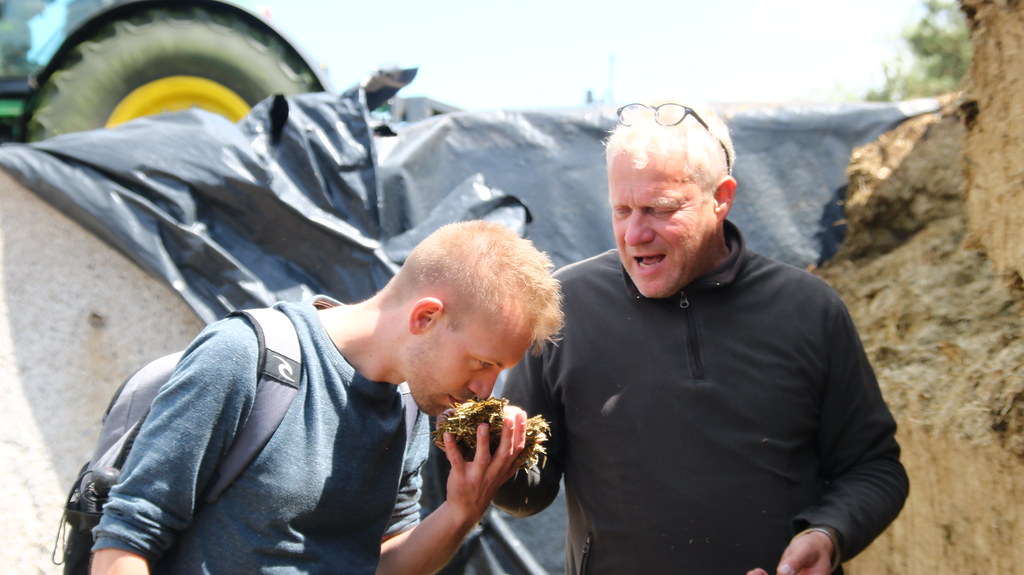 主責沼氣發電工作的Markus Rüter（右）拿牧草給翻譯夥伴Tobias Sauer（左）聞乾燥的牧草，感受牧草的清香，且沒有異味。圖片來源：陳郁玲 攝