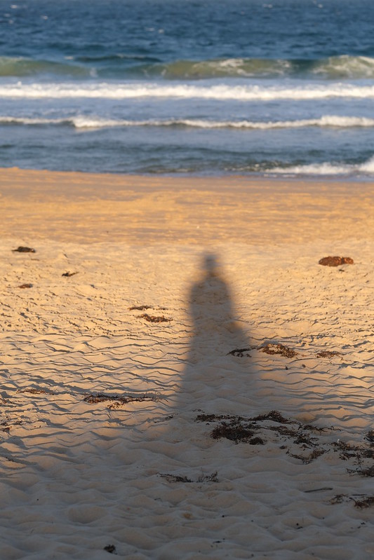 Goodbye Culburra: photograph of the photographer casting a shadow onto beach sand, out of focus waves in the distance
