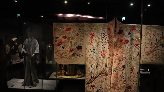 Un peignoir kimono brodé d motifs colorés sur fond ivoir, dans une vitrine