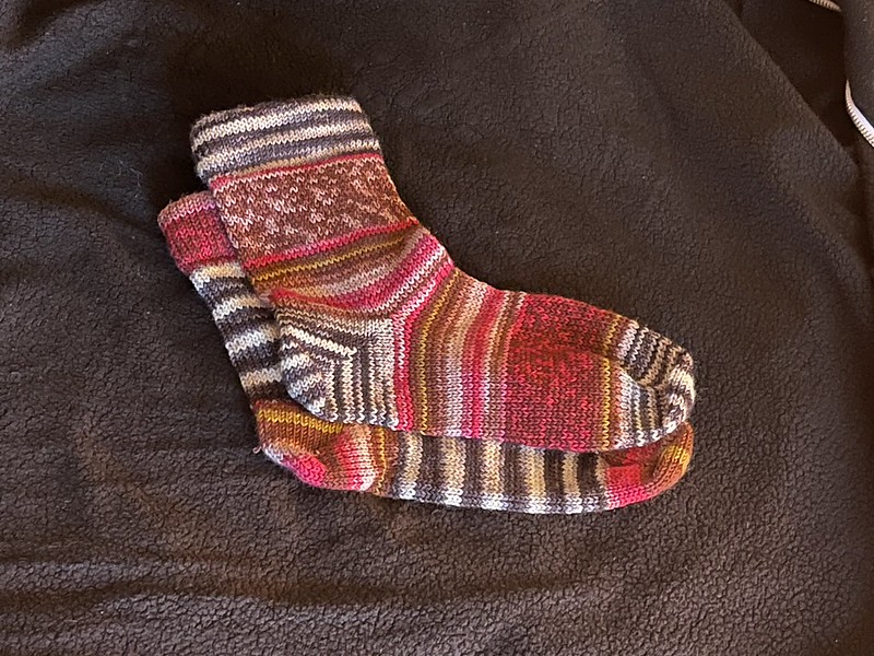 mismatched multicolored socks (one with white/black striped cuff, heel, and toe and red/pink/gold main sock body; with the other sock with red/pink/gold cuff, heel, and toe and white/black striped main sock body) that were knitted on a circular sock knitting machine