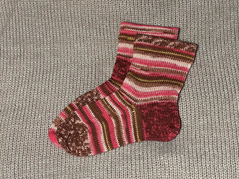 mismatched multicolored socks (both in red/pink/gold self-patterning sock yarn) that were knitted on a circular sock knitting machine