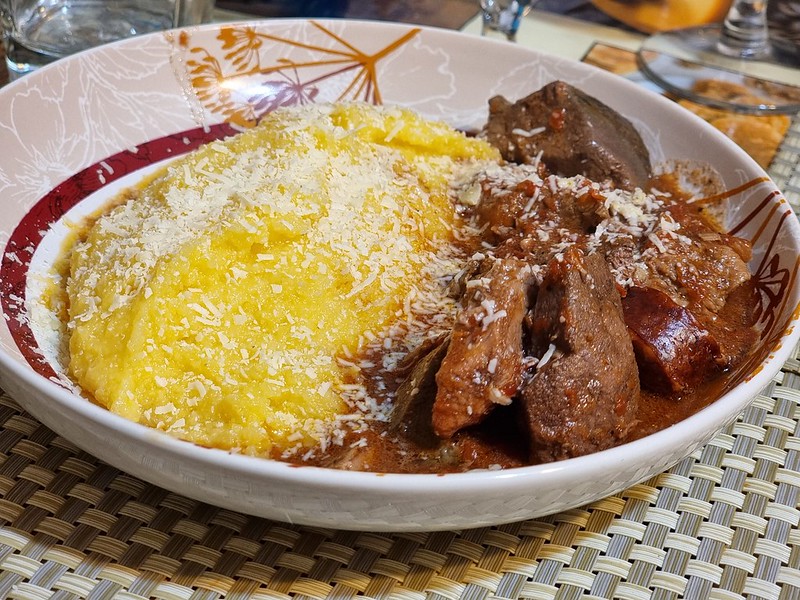 A deep plate with polenta on the left hand side and the meat stew on the right. The dish has grated cheese sprinkled on the top.