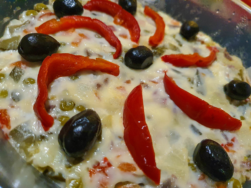 A close-up of the beef salad, decorated with slices pickled peppers and black olives. The top is covered with mayo.