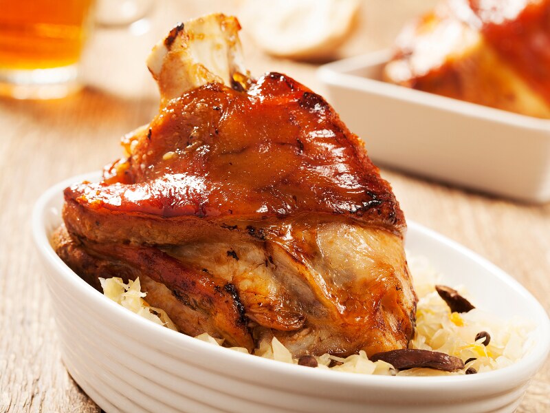 A white big deep ramekin with a pork knuckle over it. Underneath, you can see the white cabbage.