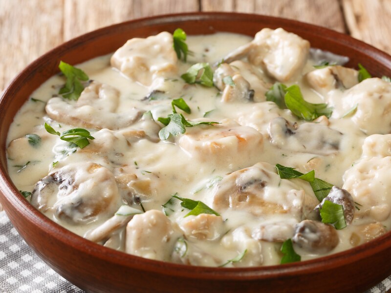  Awhite creamy dish inside a brown bowl. The dish is decorated with chopped green tarragon.