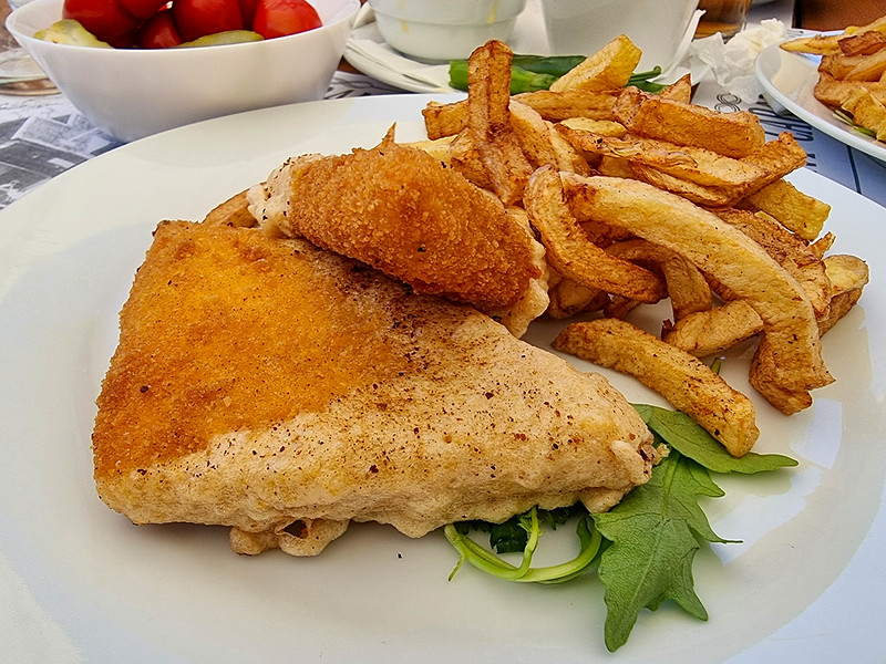 Two triangle shaped pieces of cheese deep fried, alongside fries. Underneath the cheese there are a few leaves of rocket salad.