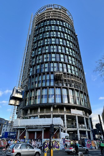 A photo of a modern, cylindrical building under construction, maybe 15 storeys tall