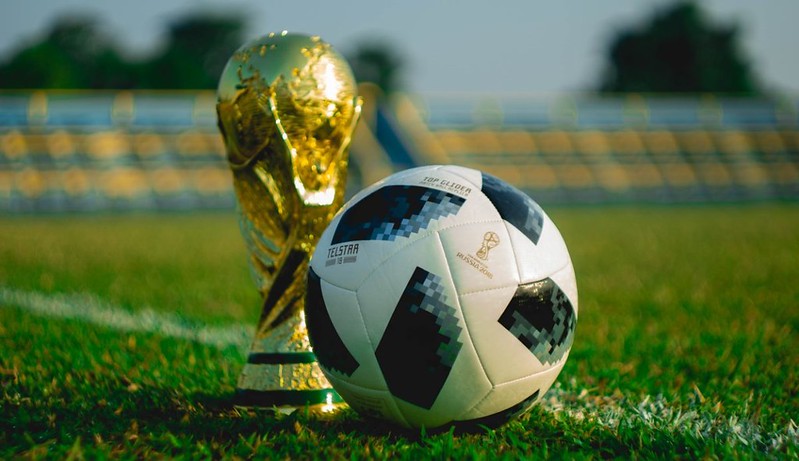 A world cup trophy and football on the grass next to each other. 