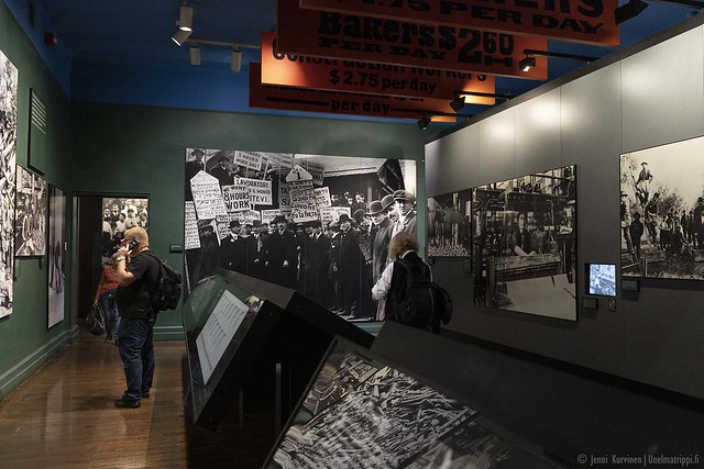 Valokuvia ja muita näyttelyesineitä ja museovieraita Ellis Islandin siirtolaismuseon näyttelyssä