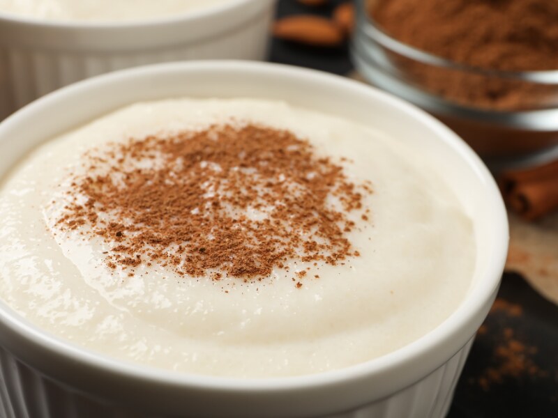 A white ramekin with the semolina pudding in it. It is decorated with cinnamon.