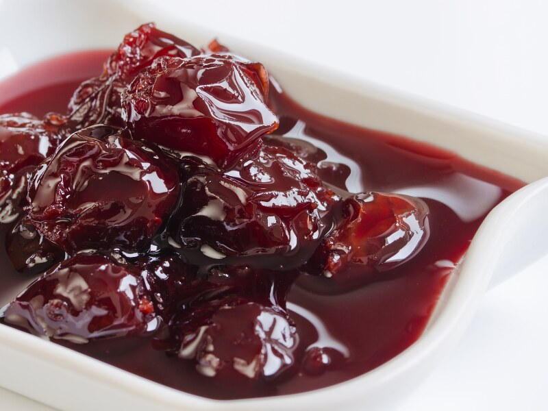 A small ramekin filled with sour cherry jam. You can see the uncut fruits inside a dark red, runny liquid.