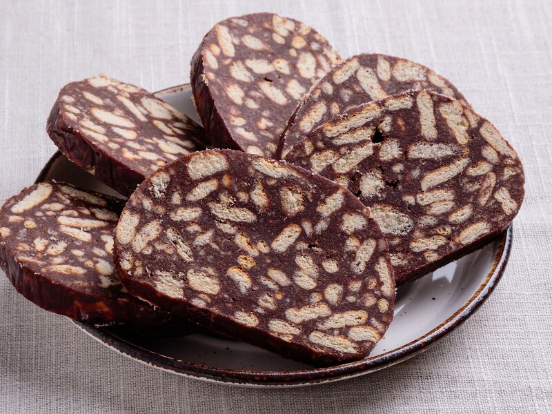 Slices of biscuit salami on a white plate. In each slice you can see the chopped biscuits surrounded by the cocoa