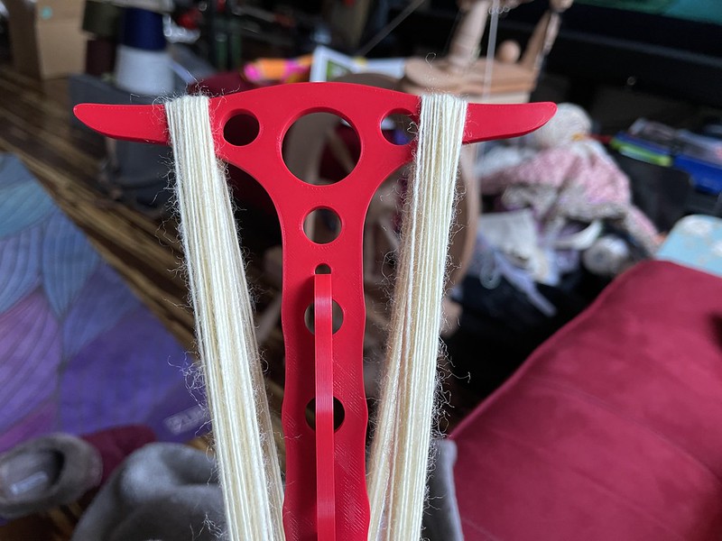 a red 3D printed niddy noddy with undyed white singles wrapped on it